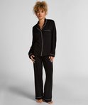Vrouw in zwarte pyjamaset met witte biezen en een witte strik op de tailleband.