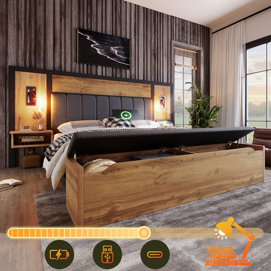 Lit double avec accents en bois, tête de lit grise, tables de chevet avec lampes, et un espace de rangement ouvert sous le lit avec des coussins.