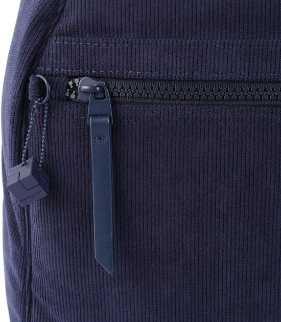 Detail van de donkerblauwe ribfluwelen rugzak: rits met blauw trekkoord en een kleine blauwe kubusvormige hanger met 'Hedgren' erop.