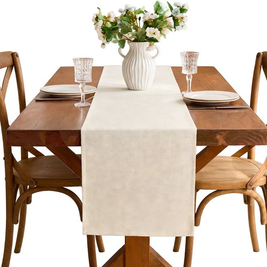 Lichtbeige linnenlook tafelloper op een houten tafel met een vaas, bloemen en glazen.