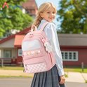 Een jong meisje met blond haar draagt een roze schoolrugzak met witte ritsen, vakken, een konijnenhanger en een geblokt patroon.