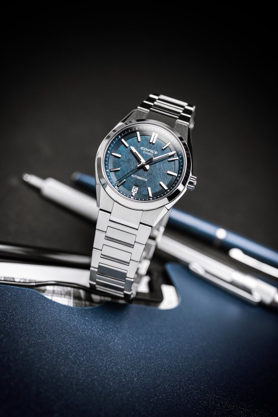 Zilverkleurig Edifice horloge met blauwe wijzerplaat, liggend op kantoorartikelen.