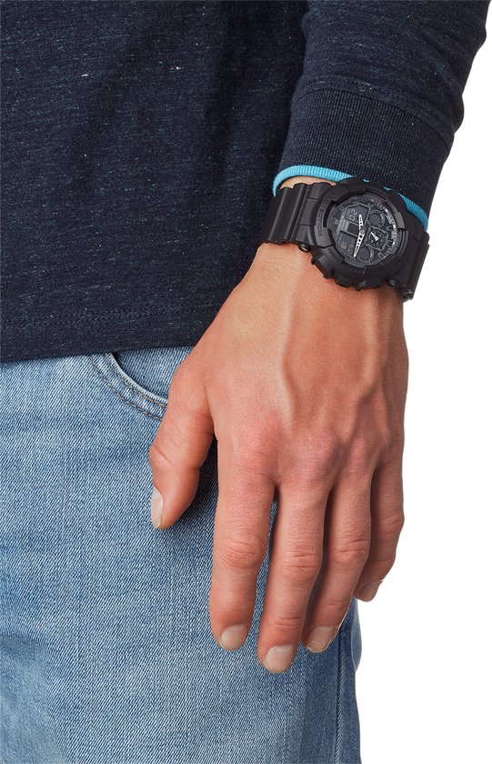 Man met spijkerbroek en donkerblauwe trui draagt een zwarte G-Shock horloge om zijn linkerpols.