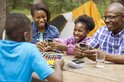 Een familie speelt UNO All Wild rond een picknicktafel in het bos, met een tent op de achtergrond.