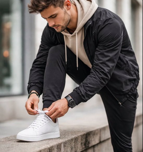 Man met witte sneakers en een zwarte jas die zijn veters strikt.
