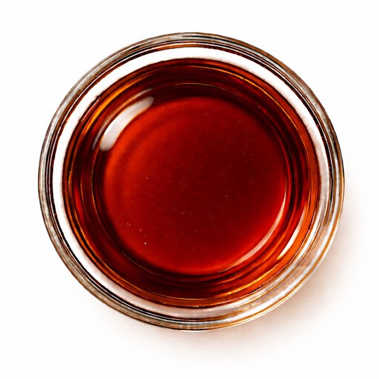 Transparant schaaltje met goudbruine frambozenolie, van bovenaf gefotografeerd.