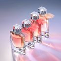 Vier glazen parfumflessen met roze en oranje vloeistof en gekleurde strikken.