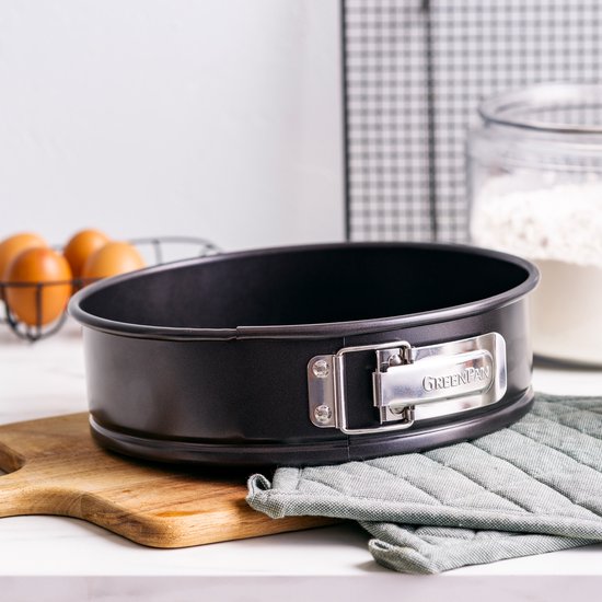 Zwarte ronde springvorm met zilverkleurige gesp en 'GREENPAN' logo, op houten plank.