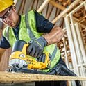 Een man met geel, groen en zwart gereedschap snijdt een plank met een DeWalt decoupeerzaag.