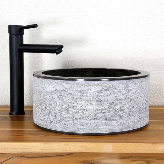 Lavabo rond en pierre naturelle grise, avec extérieur texturé et intérieur lisse, à côté d'un robinet noir.