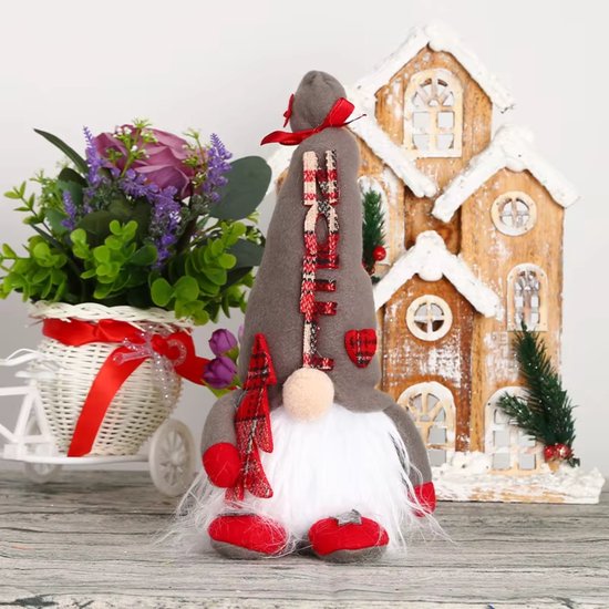 Gnome de Noël gris avec barbe blanche, écharpe à carreaux et chaussures rouges, devant une maison.
