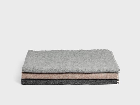 Stapel van drie wollen babydekens in grijs, beige en donkergrijs, met witte stiksels.