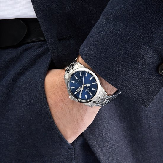 Man draagt zilverkleurige Festina horloge met blauwe wijzerplaat om de pols, onder een donkerblauw pak.