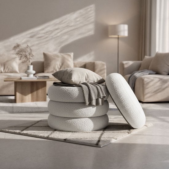Een stapel van vier ronde, witte teddy poefs met een plaid en kussen erop, in een woonkamer.