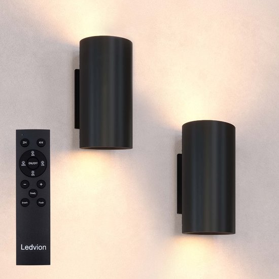 Deux appliques murales cylindriques noires sur un mur, avec une télécommande à côté.