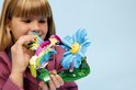 Une fille tient un colibri LEGO aux ailes vertes, jaunes et roses, près d'une fleur bleue.