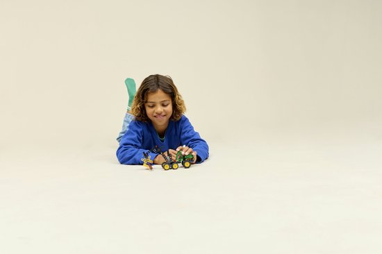 Jongen in blauwe trui speelt op de grond met LEGO Technic John Deere 1470H bosbouwmachine.