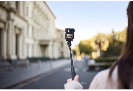 Vrouw filmt een straatscène met de DJI Osmo Nano op een selfiestick.