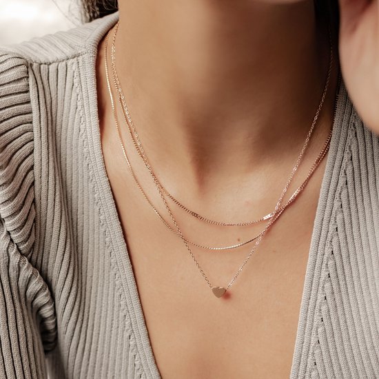 Drievoudige ketting in roségoud met kleine hartjeshanger op de borst gedragen.