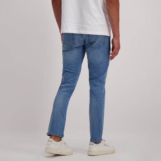 Een man met een witte t-shirt en een regular fit jeans met lichte wassing, gezien vanaf de achterkant. Hij draagt witte sneakers.
