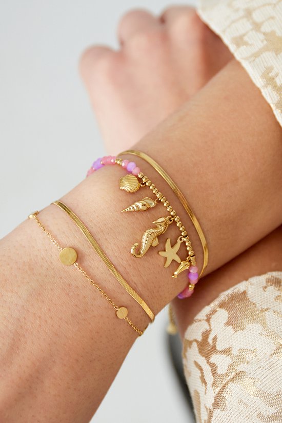 Gouden armbanden om een pols, met zeedierenbedeltjes, roze parels en cirkels.