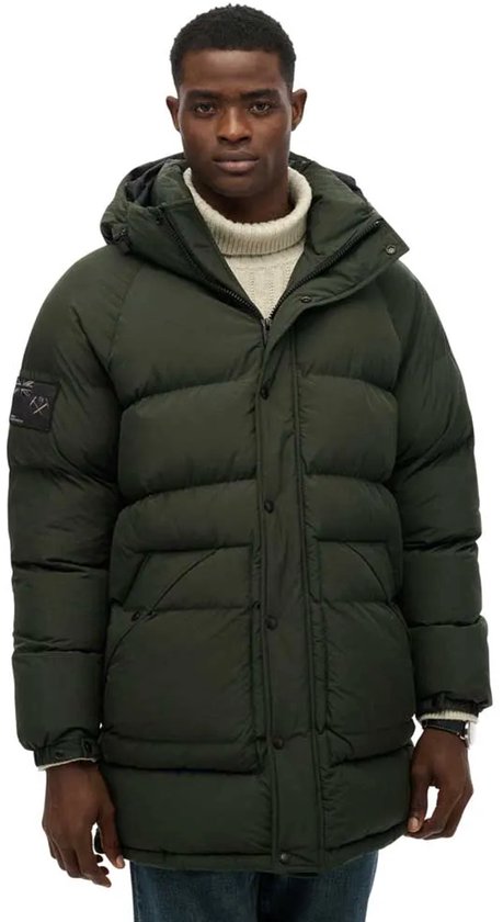 Groene lange gewatteerde parka met capuchon, gedragen door een man met coltrui.