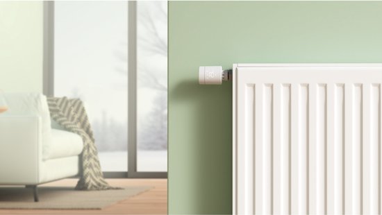 Witte radiatorthermostaat op een witte radiator in een modern interieur met een bank.