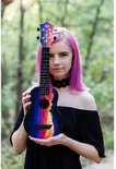 Vrouw met paars haar houdt een ukelele vast met een zonsondergangprint. De ukelele heeft blauwe, paarse, oranje en gele kleuren.