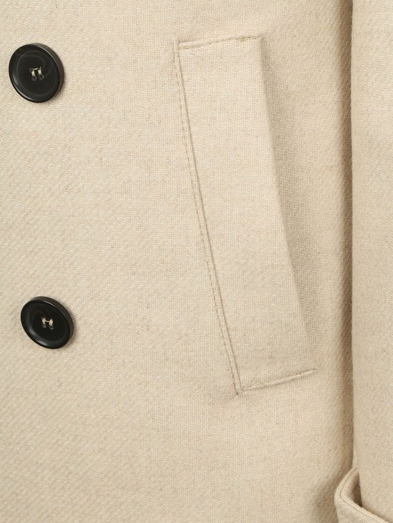 Crèmekleurige wollen jas, detail van zakopening met knopen en stiksels.
