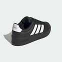 Zwarte damessneaker met dikke zool, witte Adidas-strepen op de zijkant en gouden details.