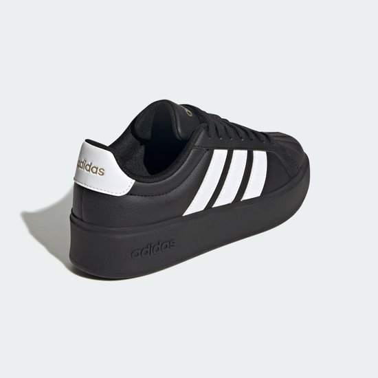 Zwarte damessneaker met dikke zool, witte Adidas-strepen op de zijkant en gouden details.