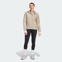 Vrouw in een beige jas met capuchon en een zwarte legging met driestrepen.