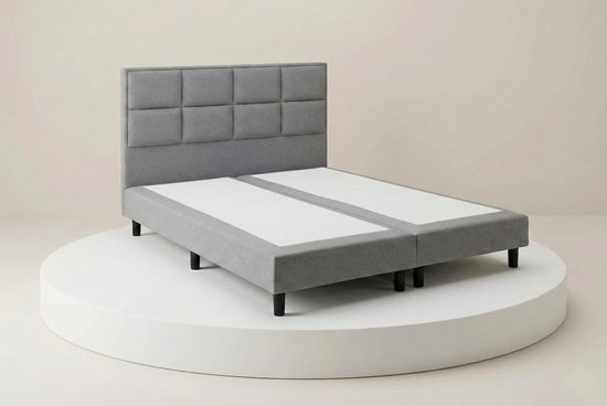 Grijze boxspring met hoofdbord van 8 vakken, twee losse bedbodems en zwarte pootjes.