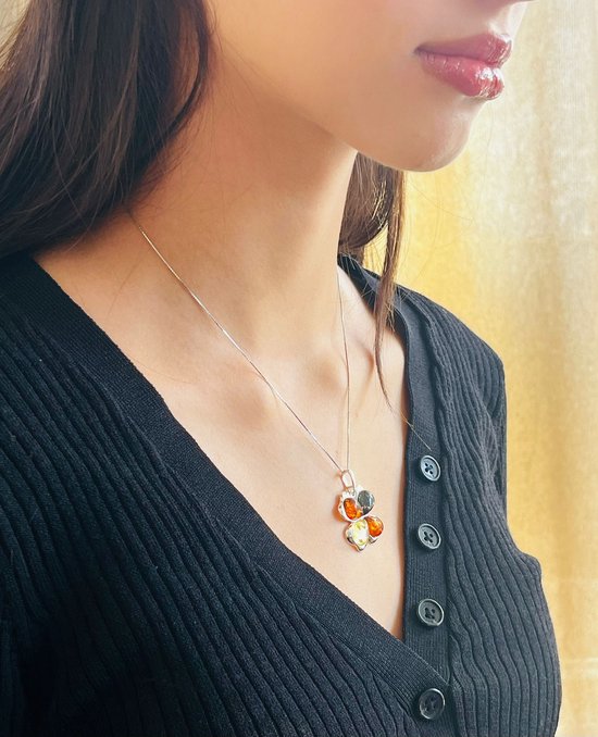 Model draagt zilveren klavertje vier hanger met oranje, gele en groene barnsteen aan een zilveren ketting.