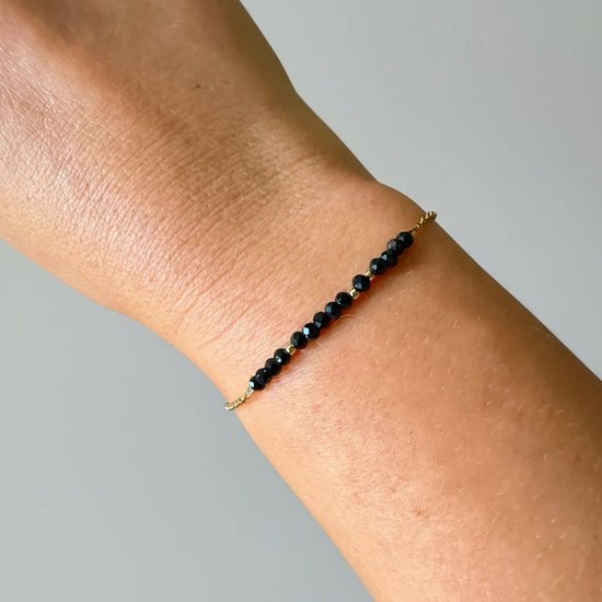 Gouden armband met zwarte toermalijn kraaltjes gedragen om een pols.