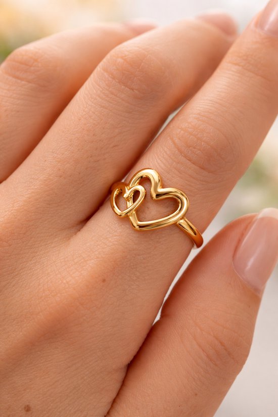 Bague dorée avec deux cœurs entrelacés, portée au doigt d'une femme.