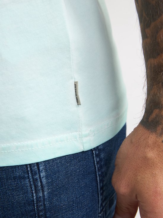 Detail van een lichtgroen T-shirt met een label "Petrol Ind.".