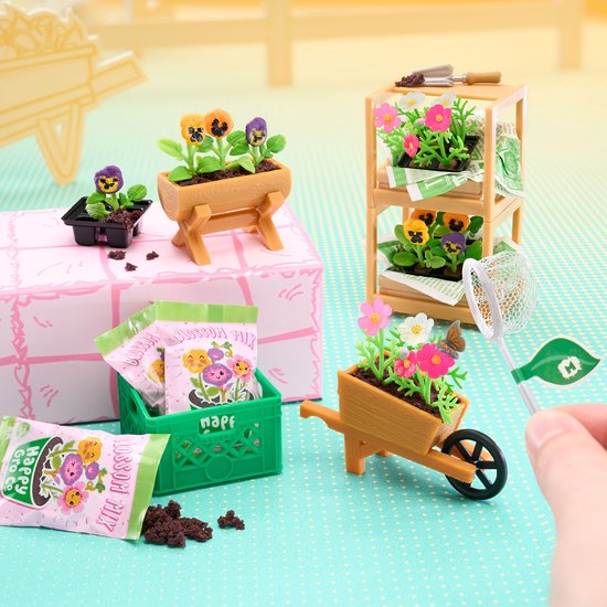 Minimodel tuin met viooltjes in plantenbak, schap en kruiwagen, naast zakjes bloemenzaad.
