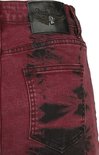 Gedetailleerde achterkant van een rode broek met zwarte batik-achtige vlekken en een logo-patch.