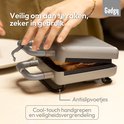 Grijze tosti-ijzer met cool-touch handgrepen en antislipvoetjes. Een hand opent de ijzer.