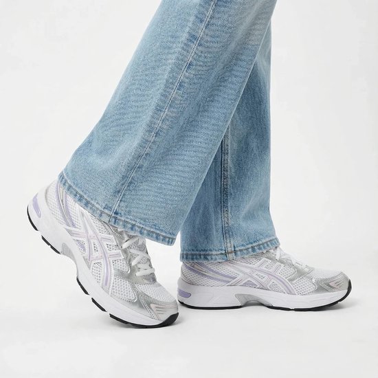 Dames voeten in Asics Gel-1130 sneakers in wit met zilverkleurige en paarse accenten, gedragen met spijkerbroek.
