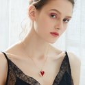 Een model draagt een gouden ketting met een rode hartvormige hanger met vleugels.