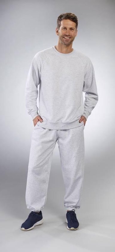 Man draagt een lichtgrijze trui met ronde hals en een lichtgrijze joggingbroek. Handen in de zakken.