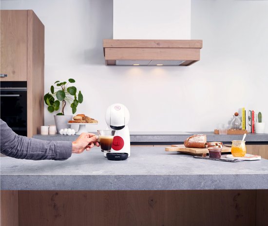 Man pakt witte Krups Piccolo XS koffiemachine met kopje koffie, brood en jam.