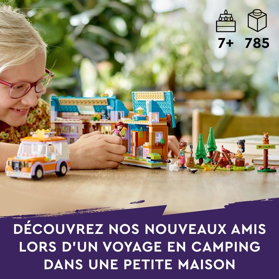 Kind met bril kijkt naar LEGO Friends set met huisje, auto, poppetjes en campfire op een tafel.