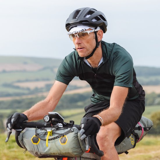 Man met helm en fietsbril fietst op een heuvel, draagt een groen shirt en zwarte handschoenen.