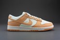 Nike Dunk Low damesschoen, wit met oranje overlays, op een grijze achtergrond.