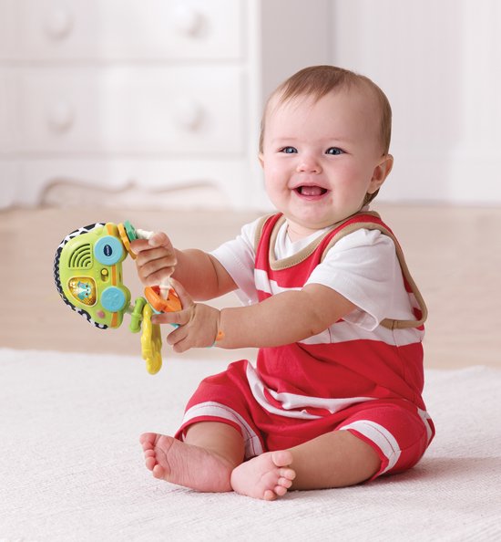 Lachende baby in rood-wit gestreept pakje speelt met groene VTech rammelsleutels.