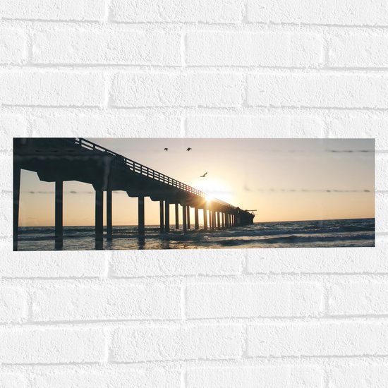 WallClassics - Muursticker - Zonnestralen door Pier boven Zee met Vogels - 60x20 cm Foto op Muursticker
