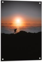 WallClassics - Tuinposter – Man lopend over Berg aan de Zee met Zonsondergang - 60x90 cm Foto op Tuinposter (wanddecoratie voor buiten en binnen)